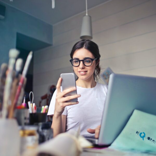 woman in white t shirt holding smartphone in front of laptop